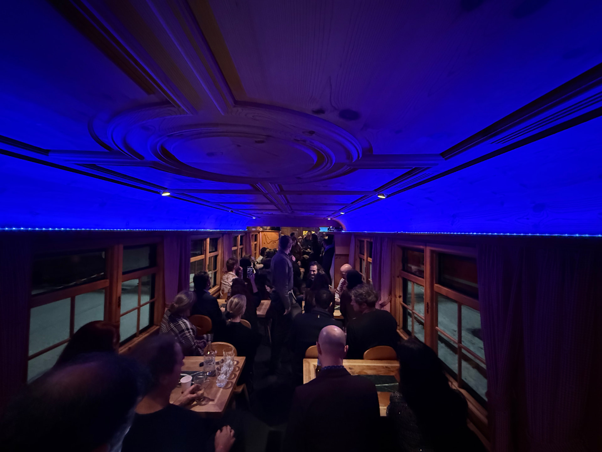 Guests filling a pine-panelled wagon under deep blue event lighting during an evening aboard