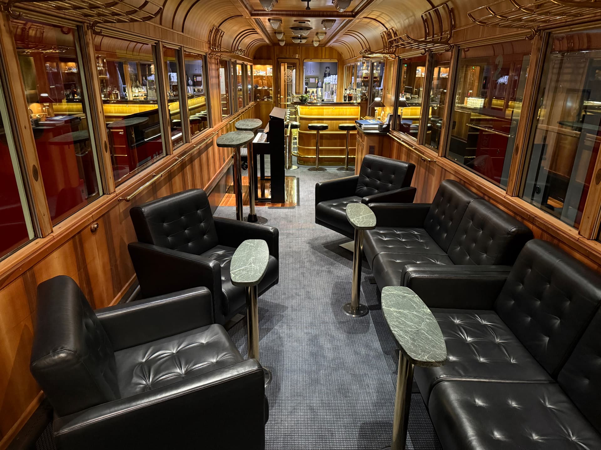 Piano Bar lounge with buttoned black leather armchairs, marble side tables and a brass-lit bar
