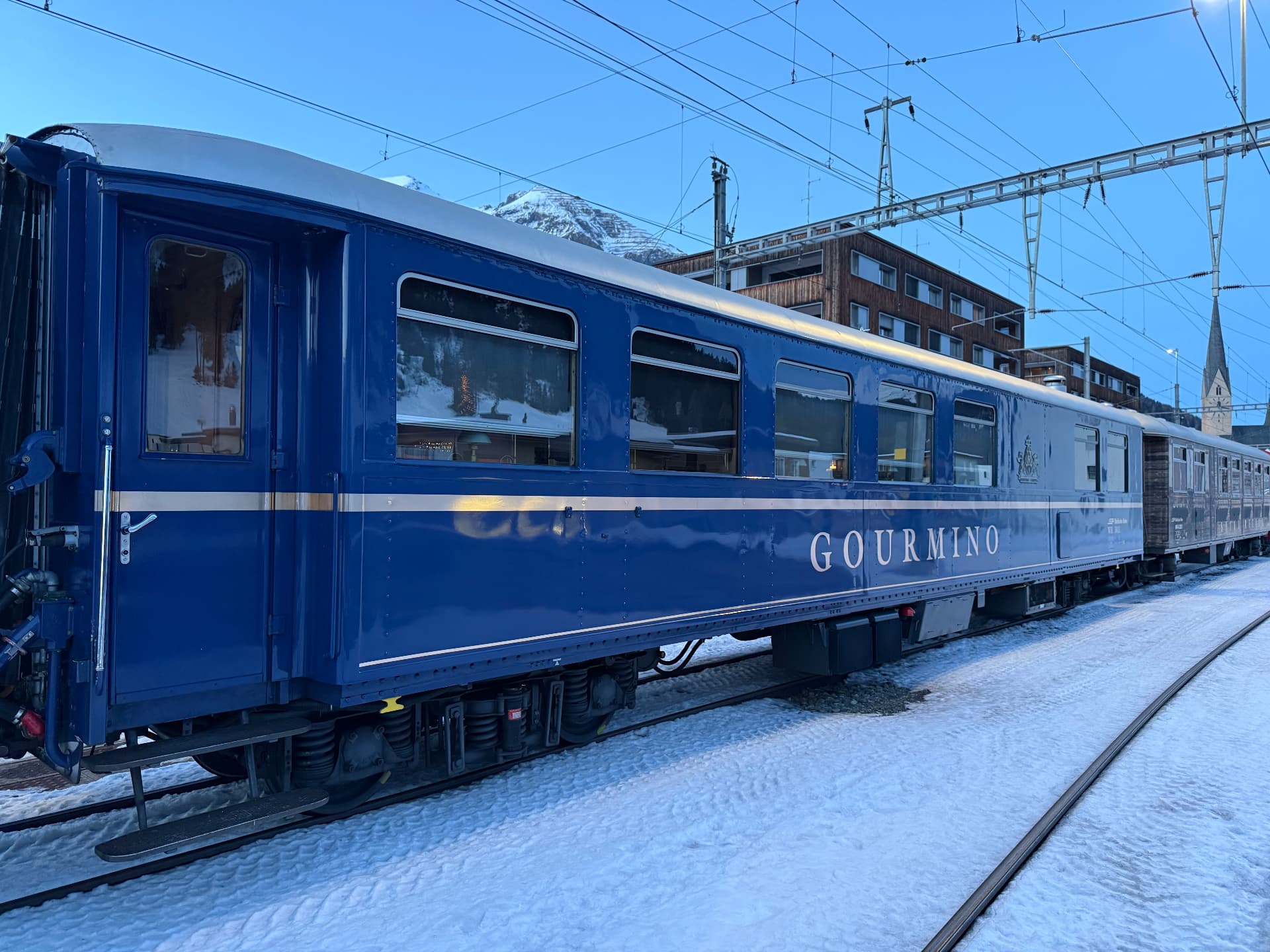 The Gourmino carriage on snowy track at dusk with Davos mountains and church tower behind