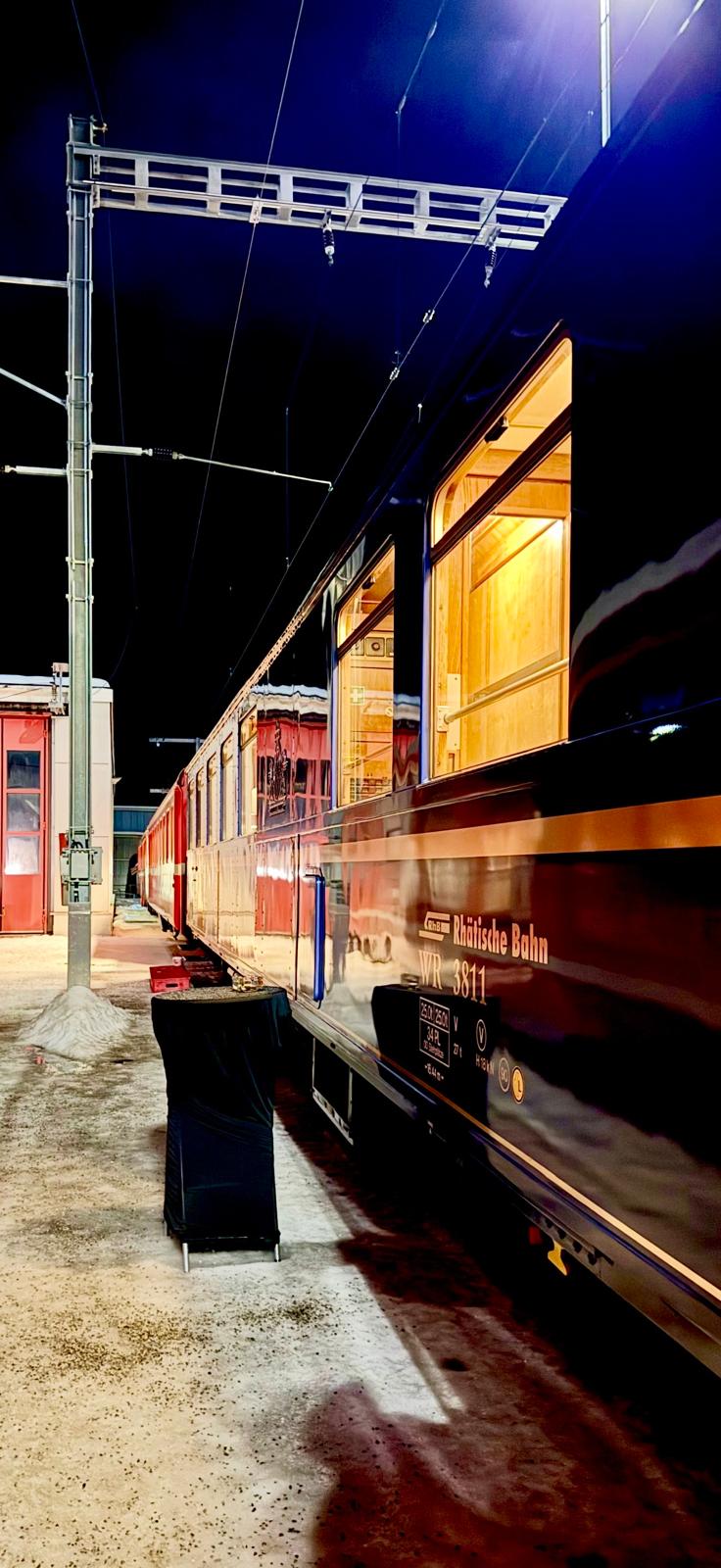 The heritage Rhaetian Railway carriages standing on snowy track at night, windows glowing warm