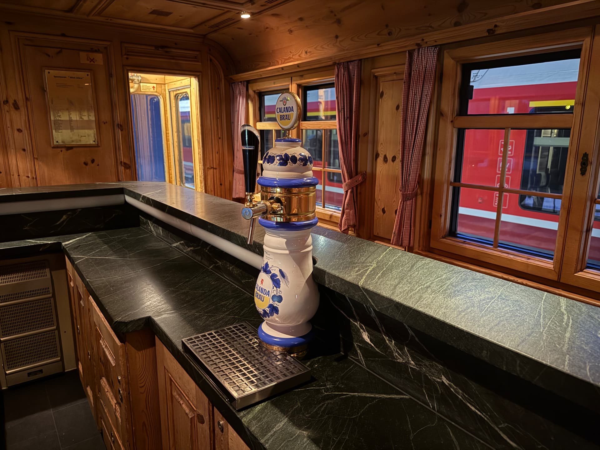 Ceramic Calanda beer tap on the Alpine Pub's dark stone bar, red gingham curtains at the windows