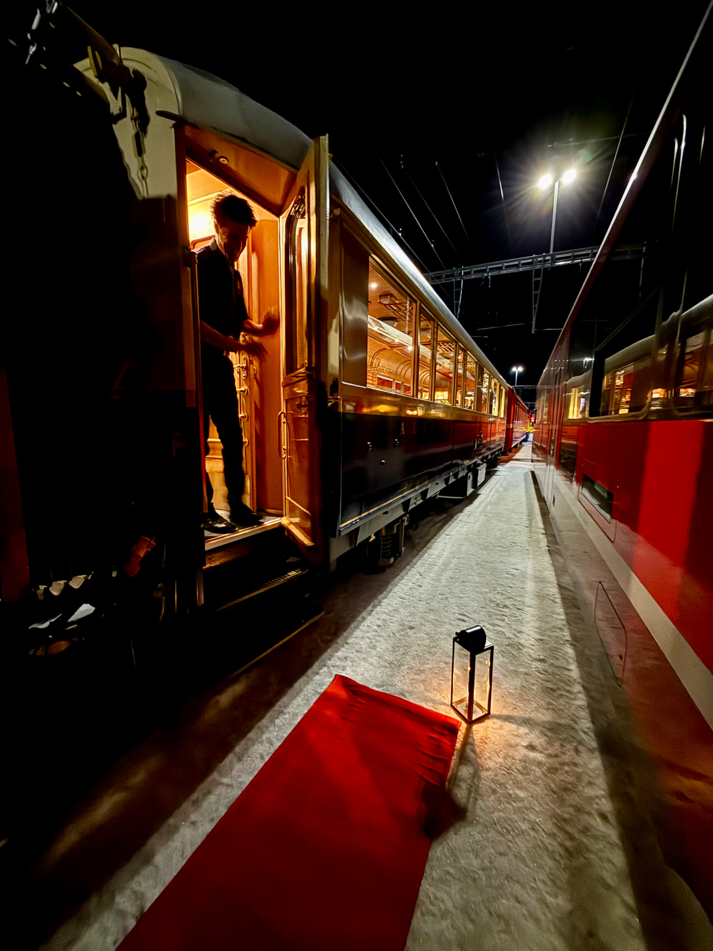 Red carpet and lantern laid in the snow at the open door of the train at night