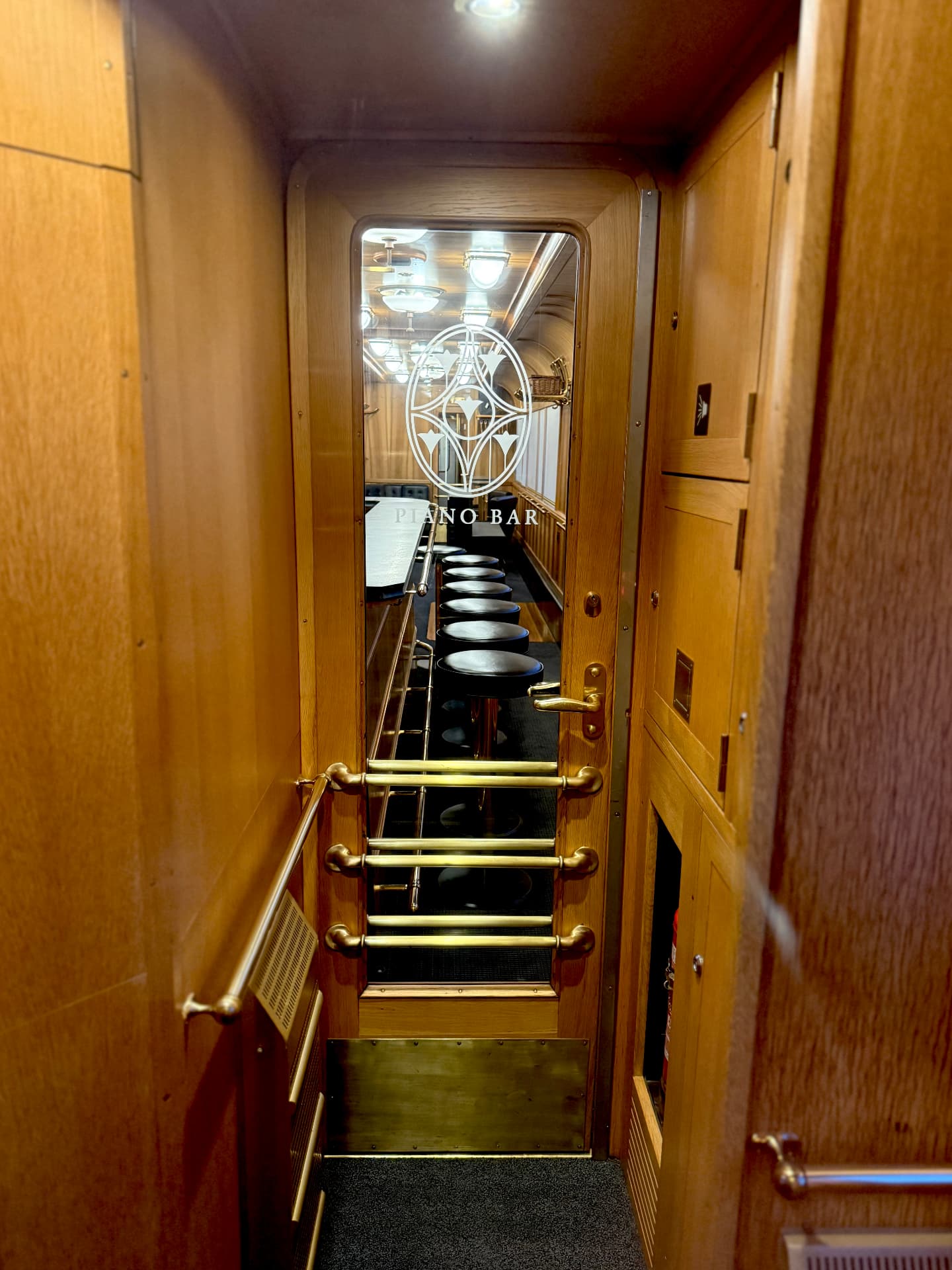 Brass-railed steps leading down through the etched Piano Bar door to the lit bar beyond