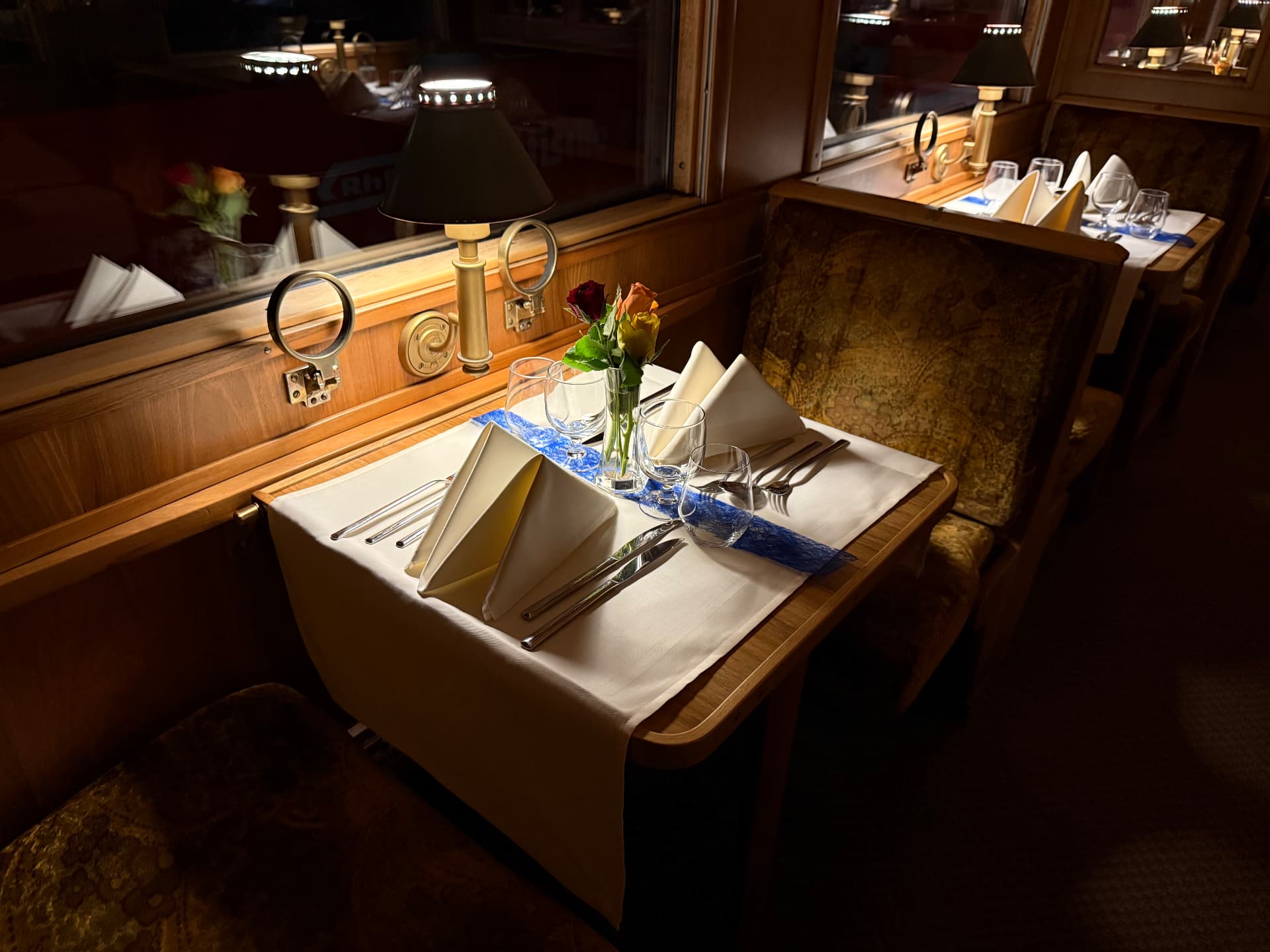 Dining table for two under a brass lamp, with roses, crystal and folded linen napkins