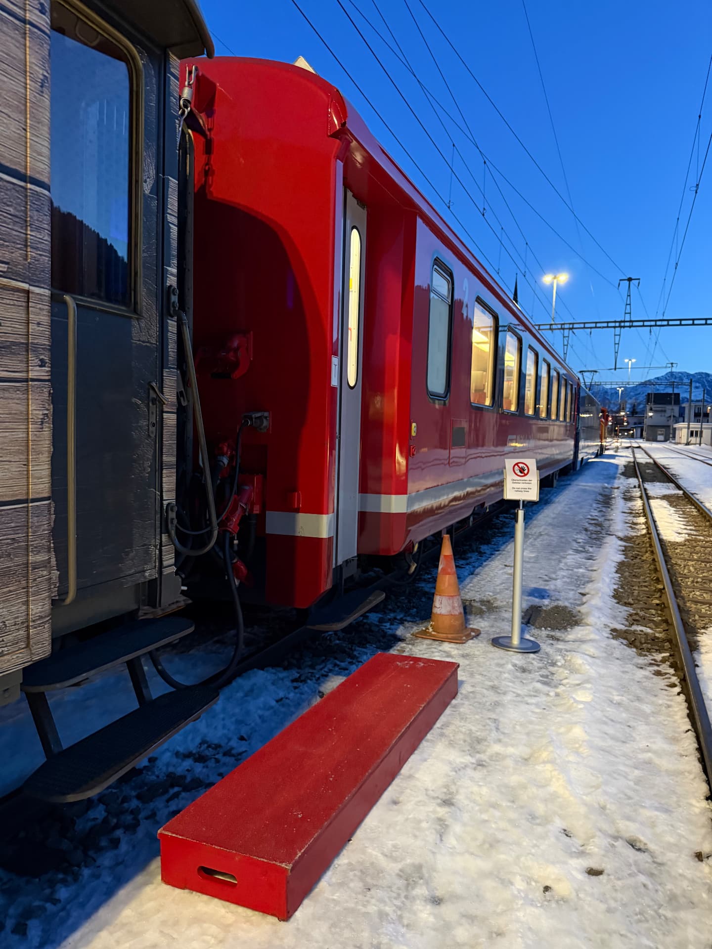 Red boarding step set out on the snowy platform beside the carriages at blue hour
