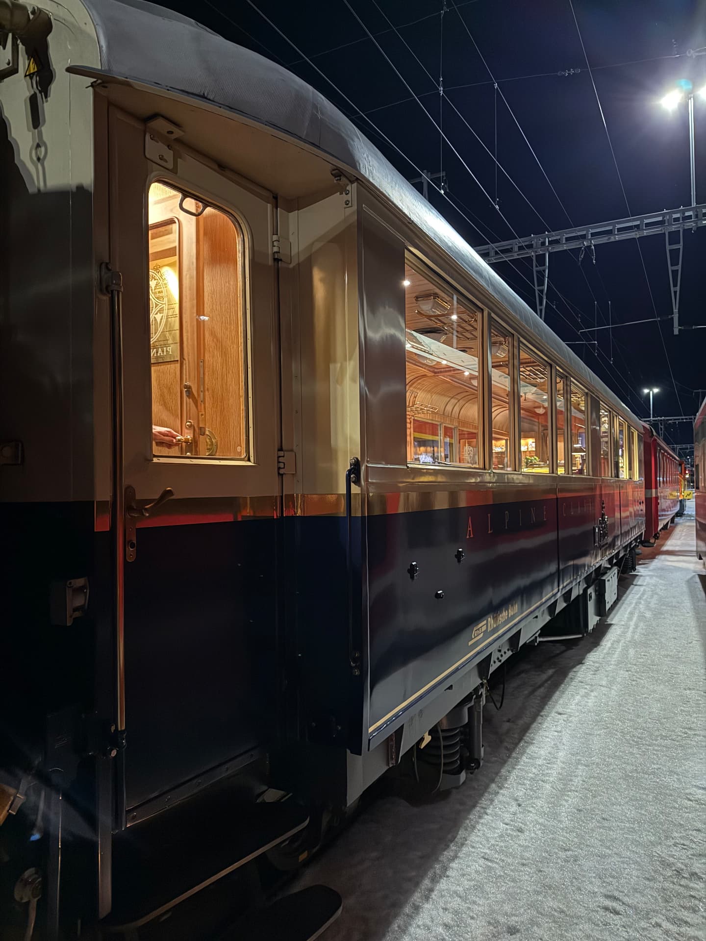 Carriage door open at night, warm light spilling onto the snow beside the lit windows