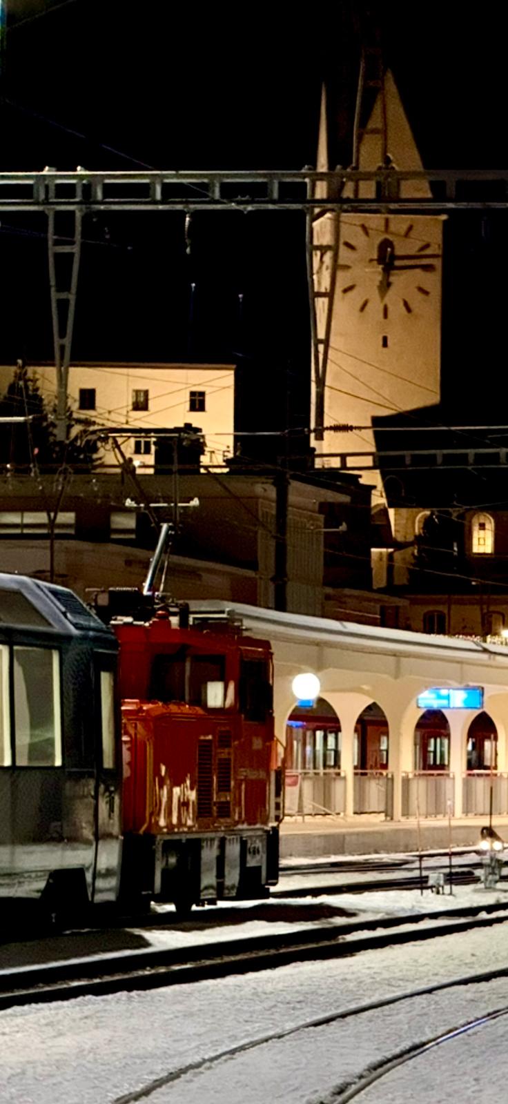 Davos Platz station at night with the illuminated church clock tower above snow-covered tracks