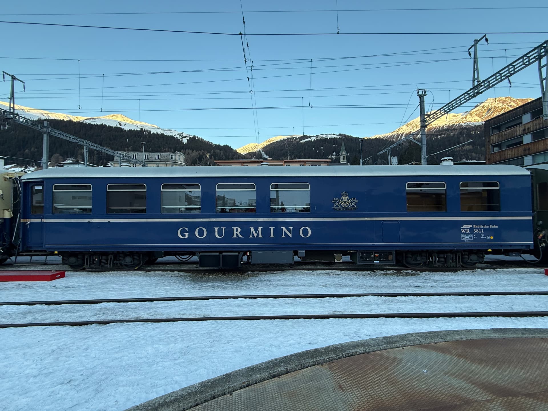 Full side view of the blue Gourmino dining carriage with sunlit Davos peaks behind