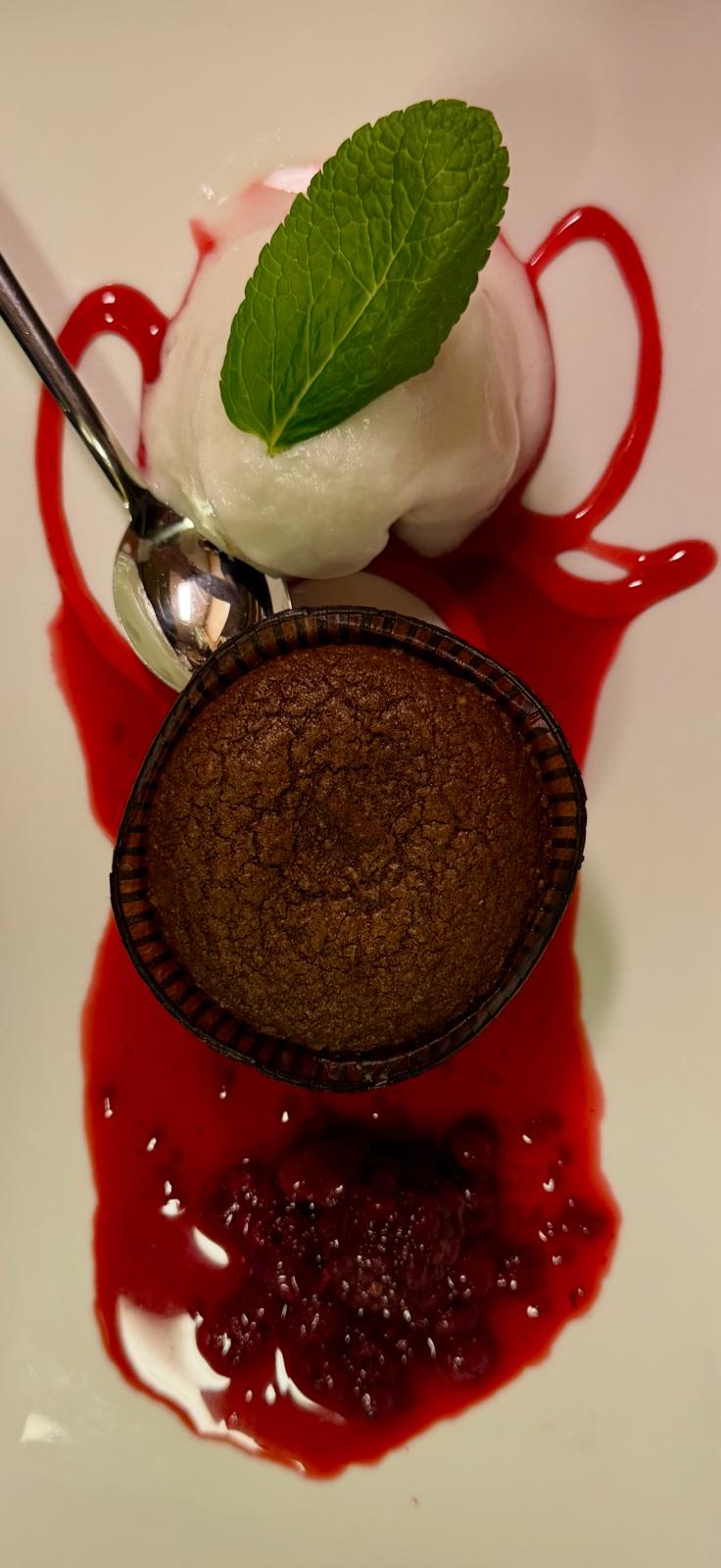 Warm chocolate fondant with sorbet and berry coulis plated on white porcelain