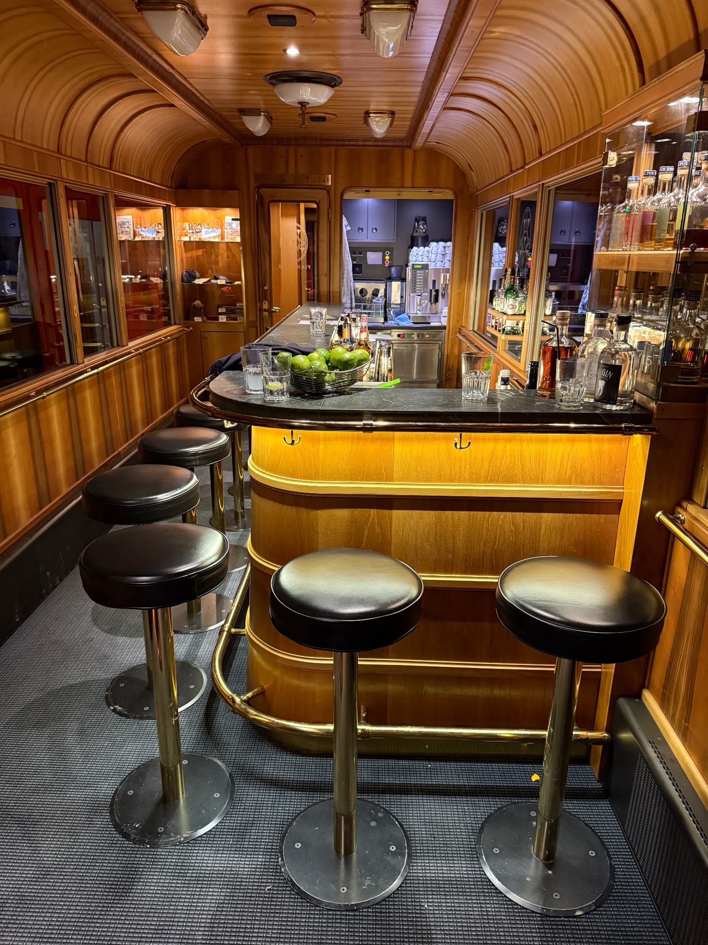 Curved marble bar counter with brass rail, leather stools and bottles behind glass