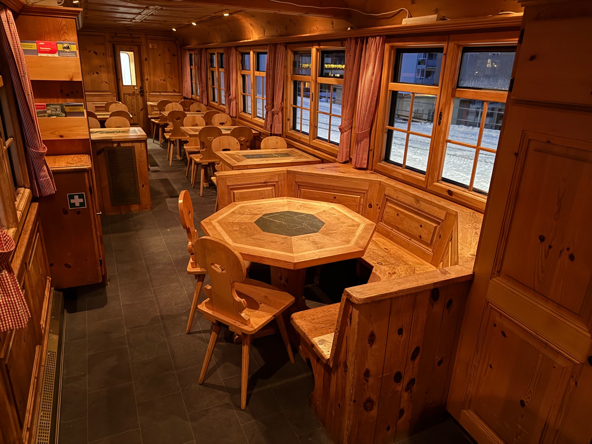 Alpine Pub seating with carved Swiss chairs, corner benches and snowy tracks through the windows