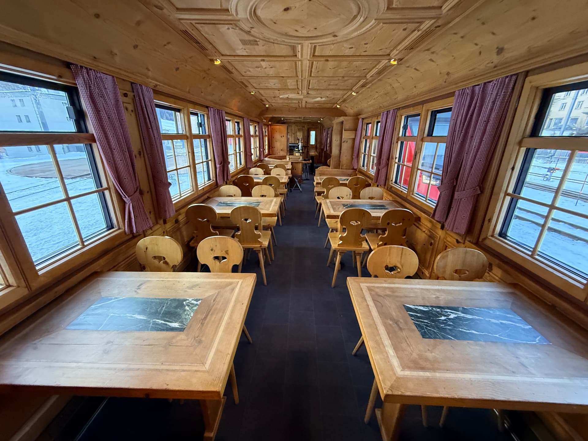 Pine-panelled wagon with carved Swiss chairs, marble-inlaid tables and red gingham curtains