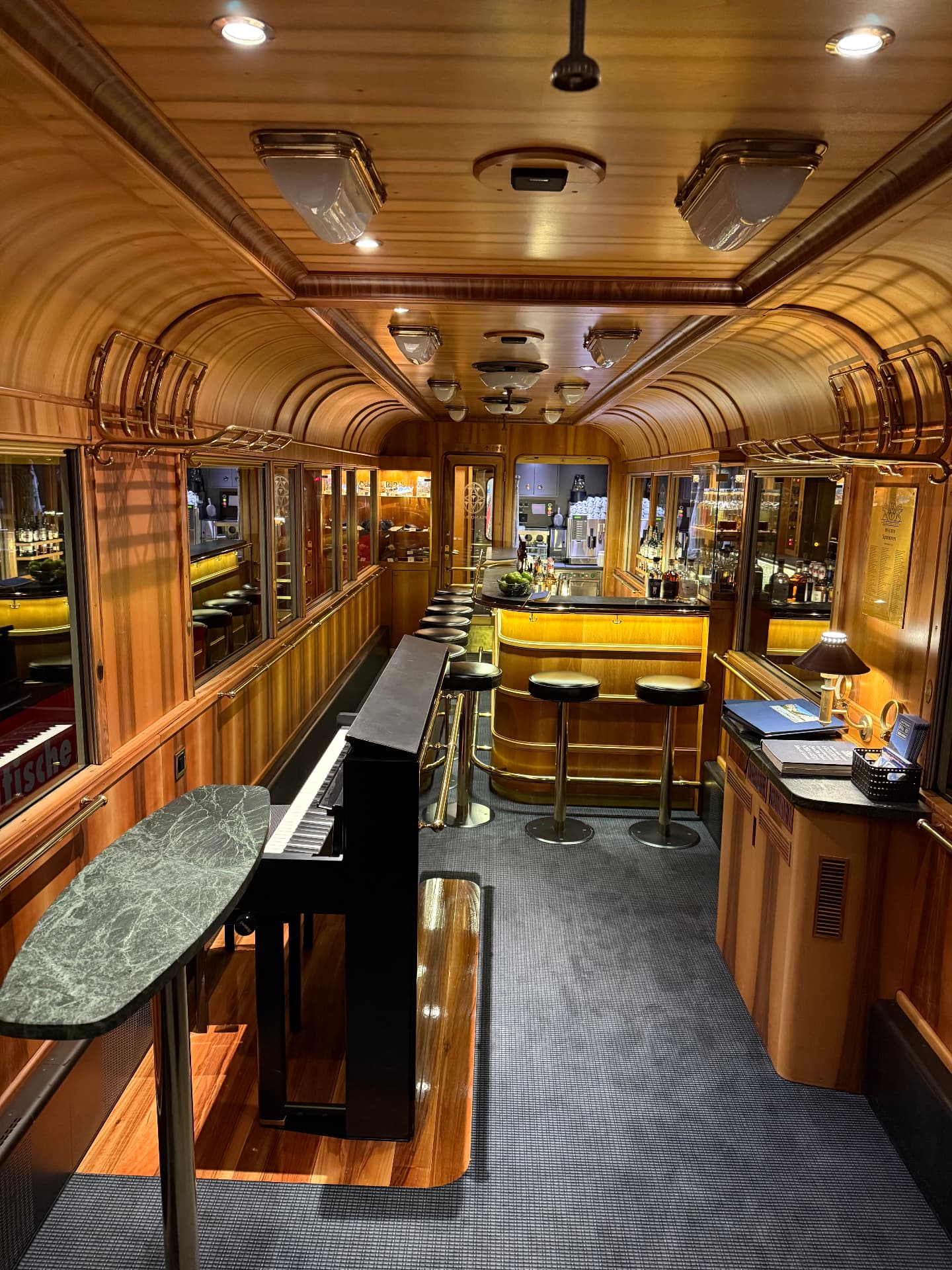 Upright piano and curved brass bar counter with stools inside the Piano Bar wagon