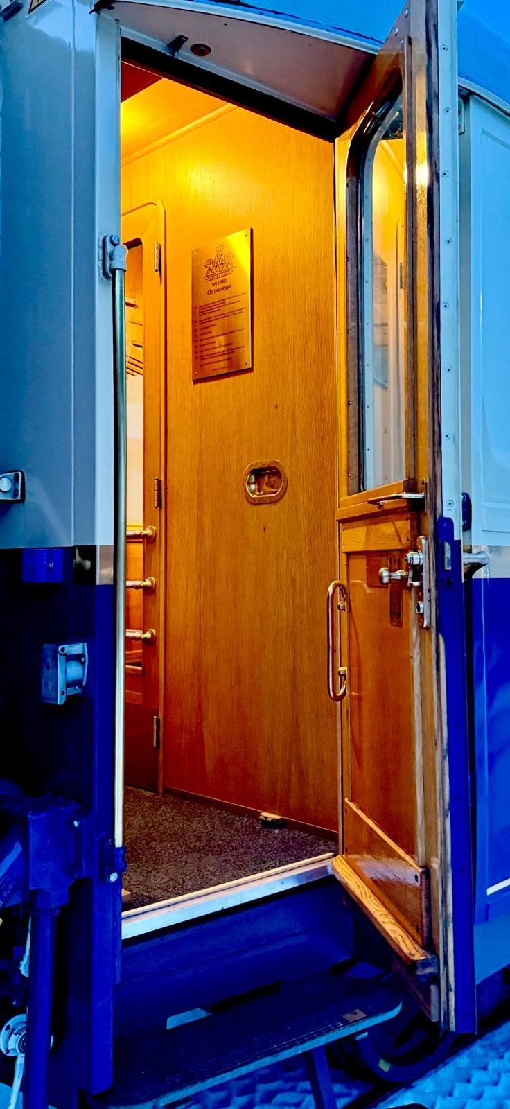 Open blue and wood carriage doorway with brass handrails and a warmly lit vestibule
