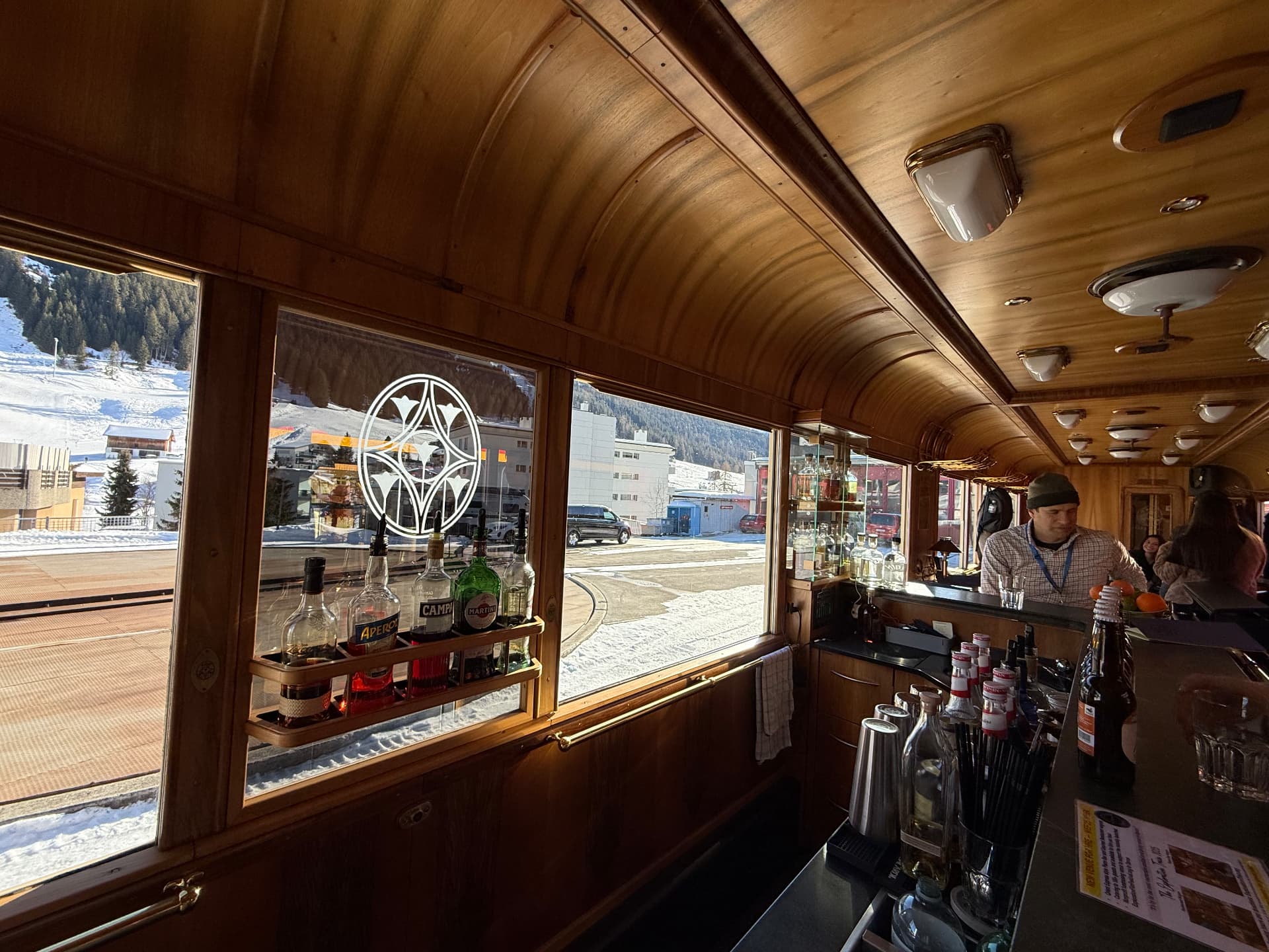 Bar counter in daylight with bottles on the window rail and snowy Davos beyond the glass