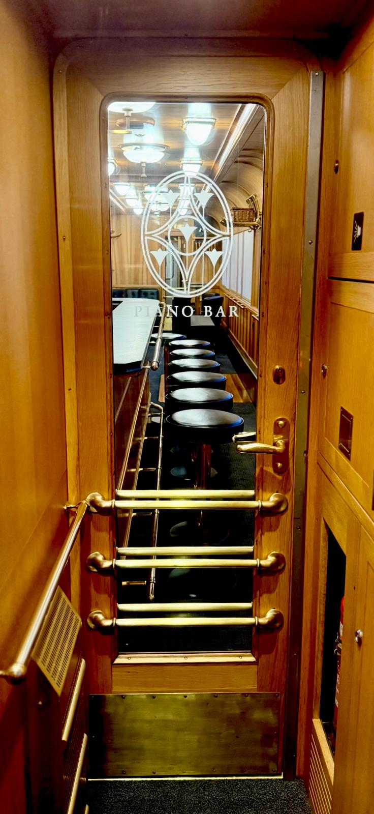Glass door etched with Piano Bar, brass handrails and steps leading down to a row of bar stools